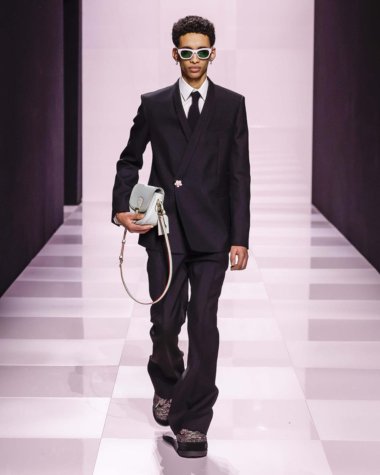 سيّد المناسبات واللحظات الراقية... هكذا هو الأسود، الذي يفيض جمالًا بأسلوب Louis Vuitton، وينسكب بعظمة على هذا الطقم المنفّذ بمهارة، والذي يزيّن سترته المميّزة زرّ أنيق على شكل زهرة