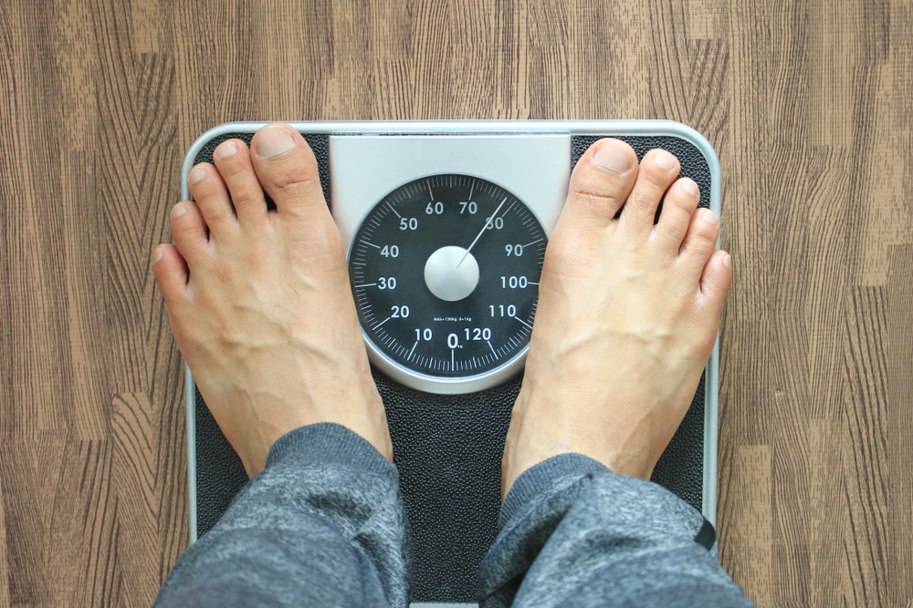 رجل يقف على ميزان تعبيرية عن اكتساب الوزن من جديد أحد مخاطر فقدان الوزن السريع