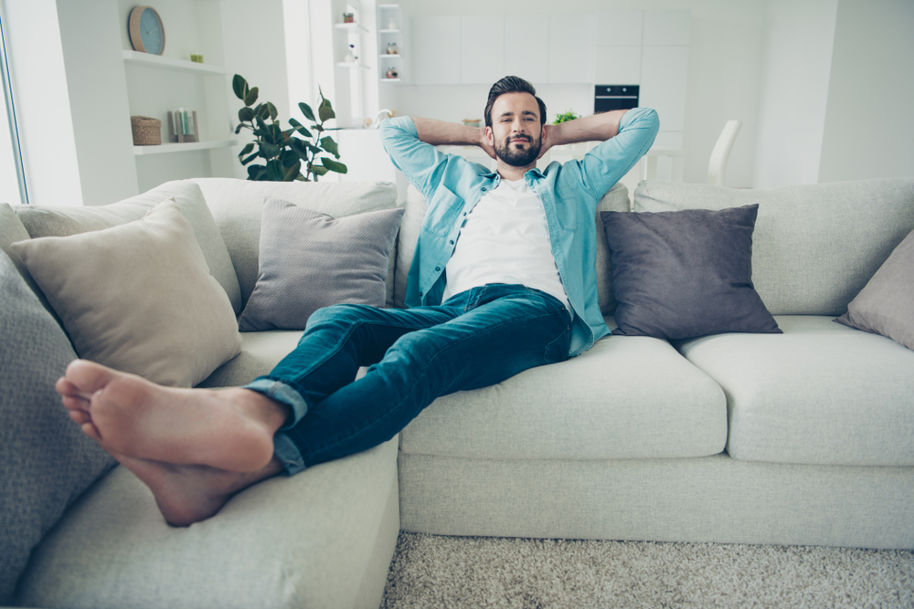 رجل يجلس مستلقيًا على أريكة تعبيرية عن الراحة ضمن طريقة رايس لعلاج التهاب وتر أخيل في المنزل