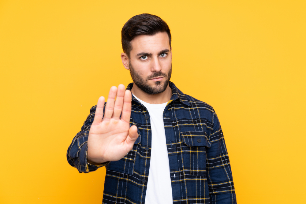 رجل يلوّح بيده للرفض تعبيرية عن وضع حدود وتعلّم قول "لا" للتخلص من عقدة المنقذ