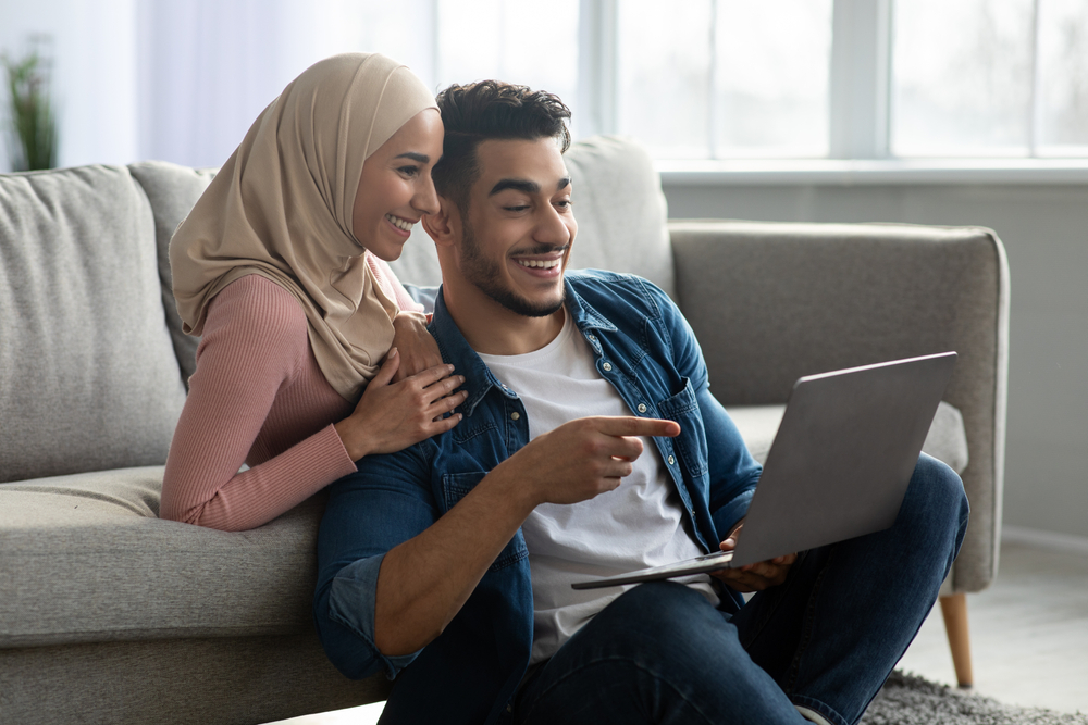 زوجان سعيدان ينظران إلى شاشة اللاب توب تعبيرية عن مشاركة التجارب للاستفادة من التكنولوجيا في تعزيز العلاقة بين الزوجين