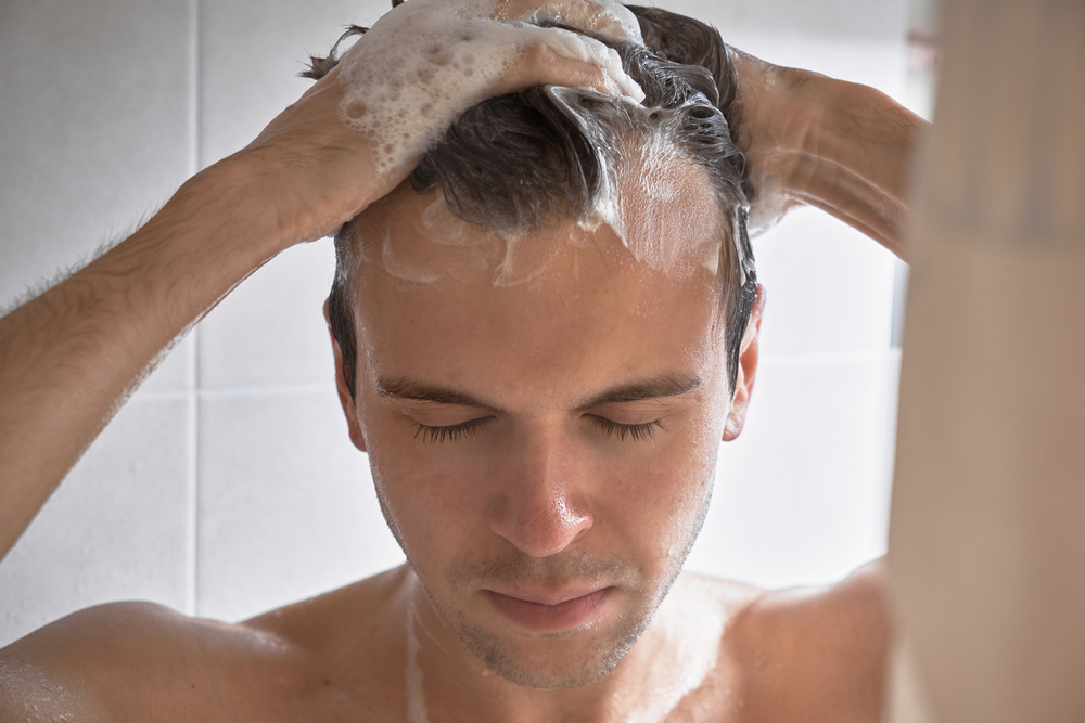 رجل يغسل شعره بالشامبو تعبيرية عن اختيار الشامبو ذي المكونات الطبيعية