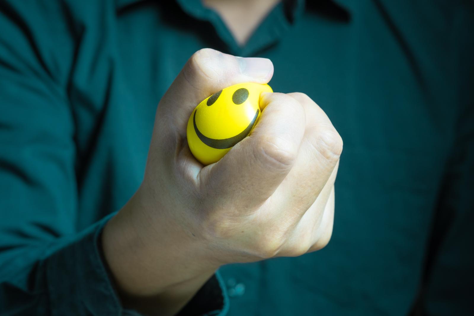 رجل يضغط بقبضته على كرة مطاطية تعبيرية عن الفرق بين كبت المشاعر وإدارتها